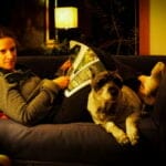 woman reading a magazin laying on the couch with her dog