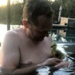 a man in the outdoors pool holding a yellow duckling