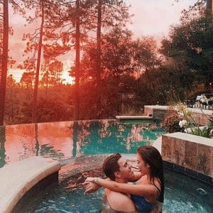 a couple of influencers hugging each other in the hut tub in the middle of the woods